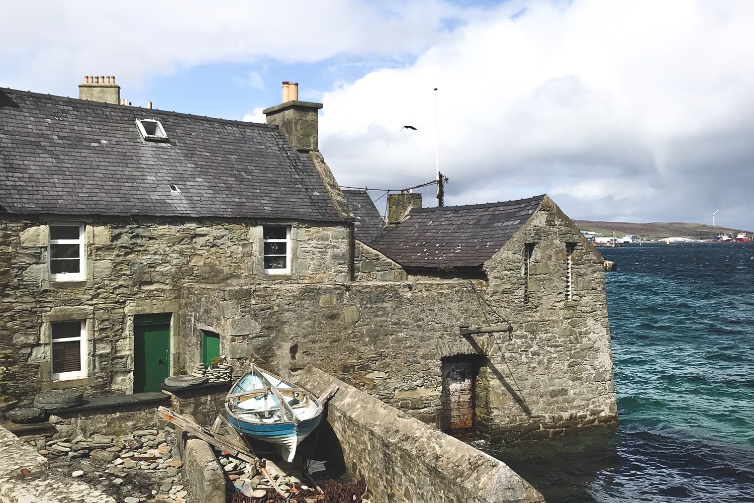 Image of a stone building, with iconic green door and blue boat showing a famous location from a the popular TV series Shetland.