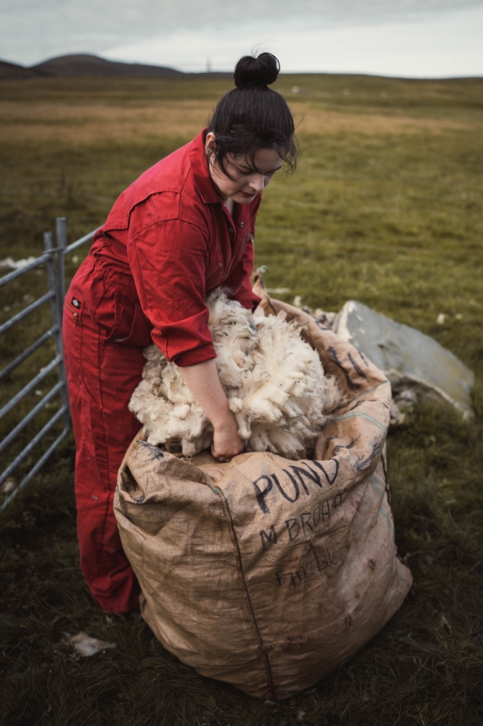 Marie Bruhat standing in a field wearing a red jumpsuit, pushing wool into a large bag.