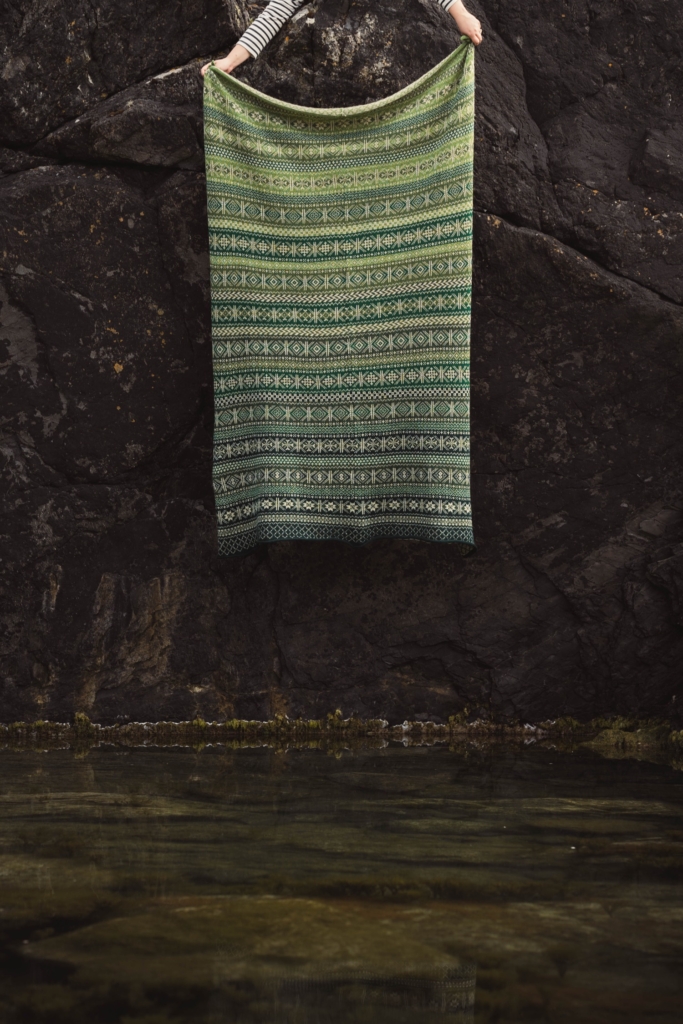 A gorgeous green Fair Isle Knitted Blanket photographed against a rocky background